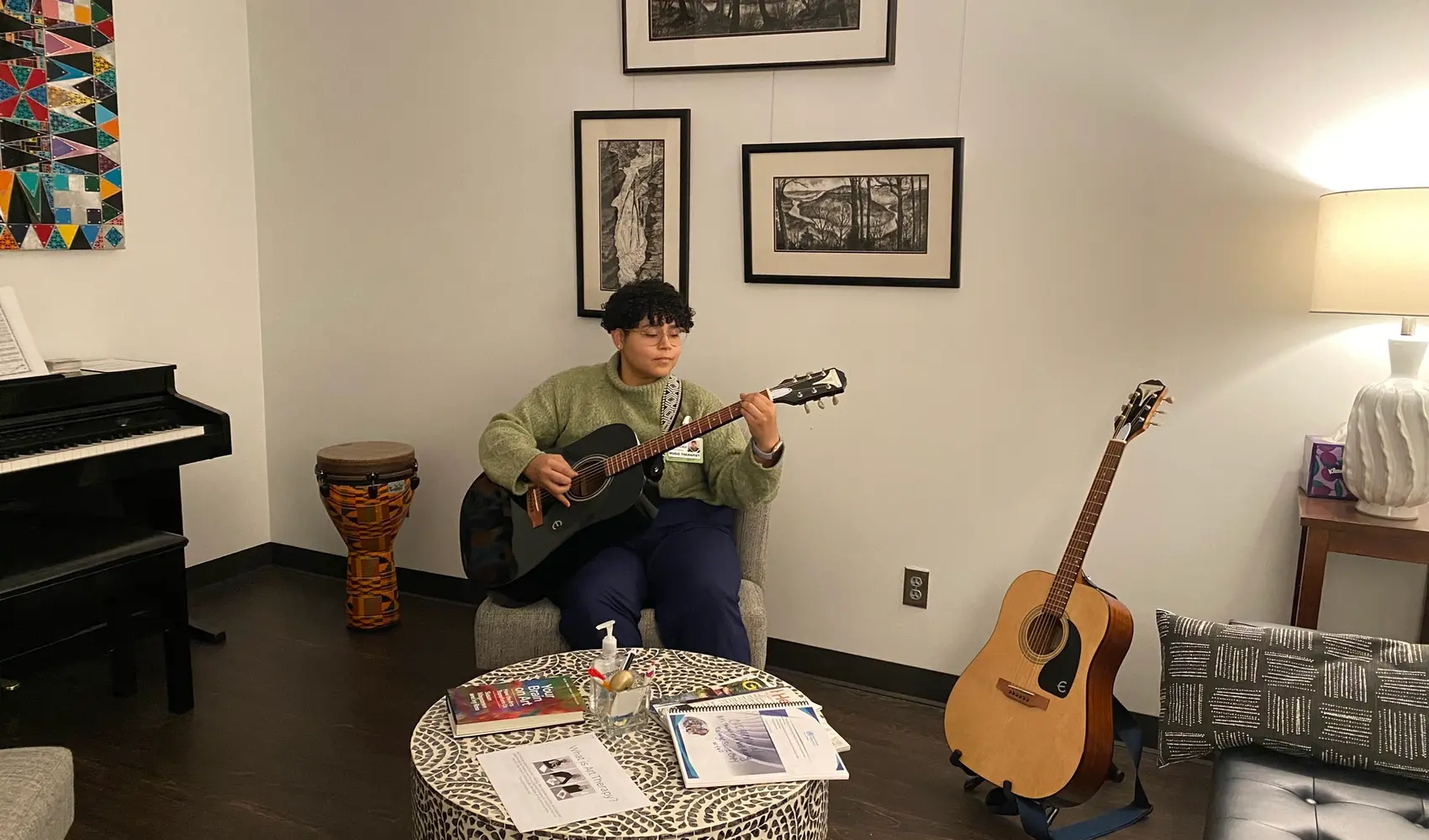 A person playing guitar and sitting in a room surrounded by musical instruments.