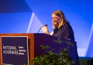 A woman stands at a podium with a sign that reads "National Academies of Sciences, Engineering, and Medicine."